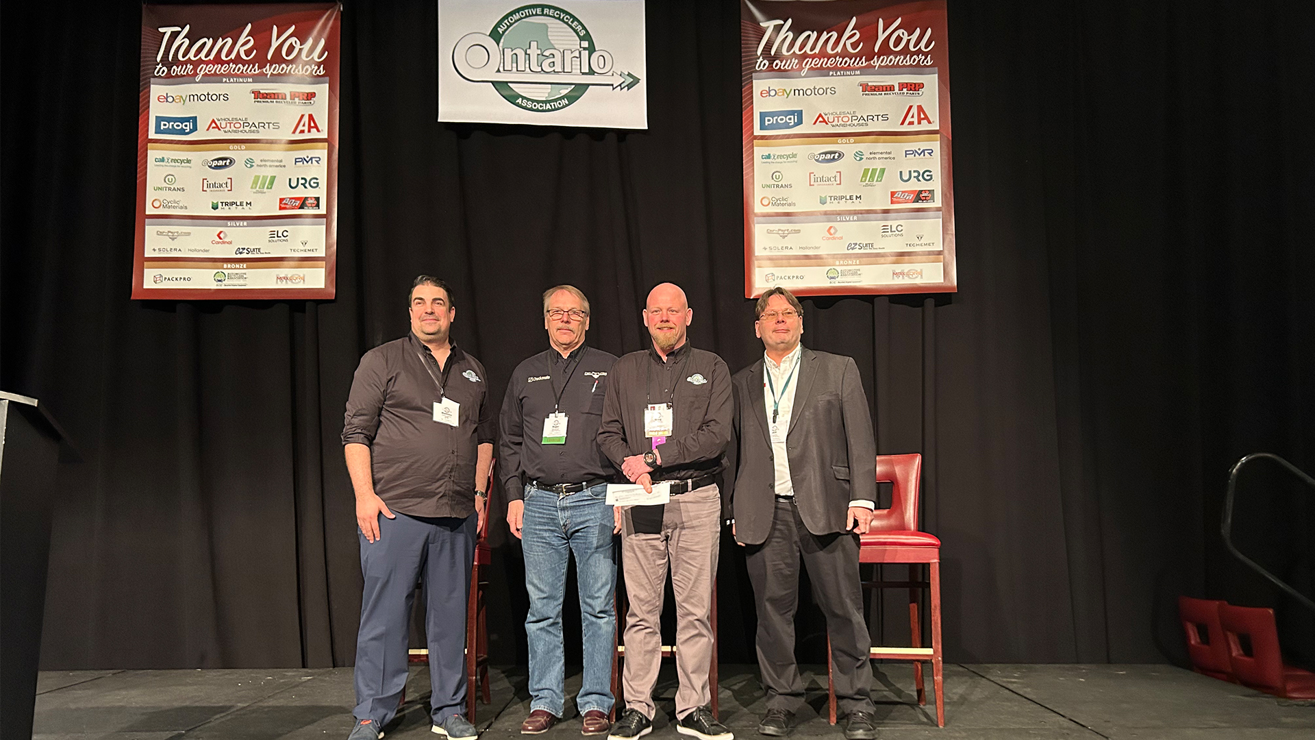 Four professionals on stage at Ontario conference with sponsor recognition boards
