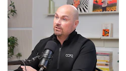 Bald podcaster speaking into microphone wearing CCPQ branded jacket