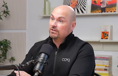 Bald podcaster speaking into microphone wearing CCPQ branded jacket
