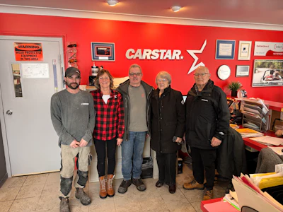 CARSTAR automotive service team standing in front of red branded wall with company logo