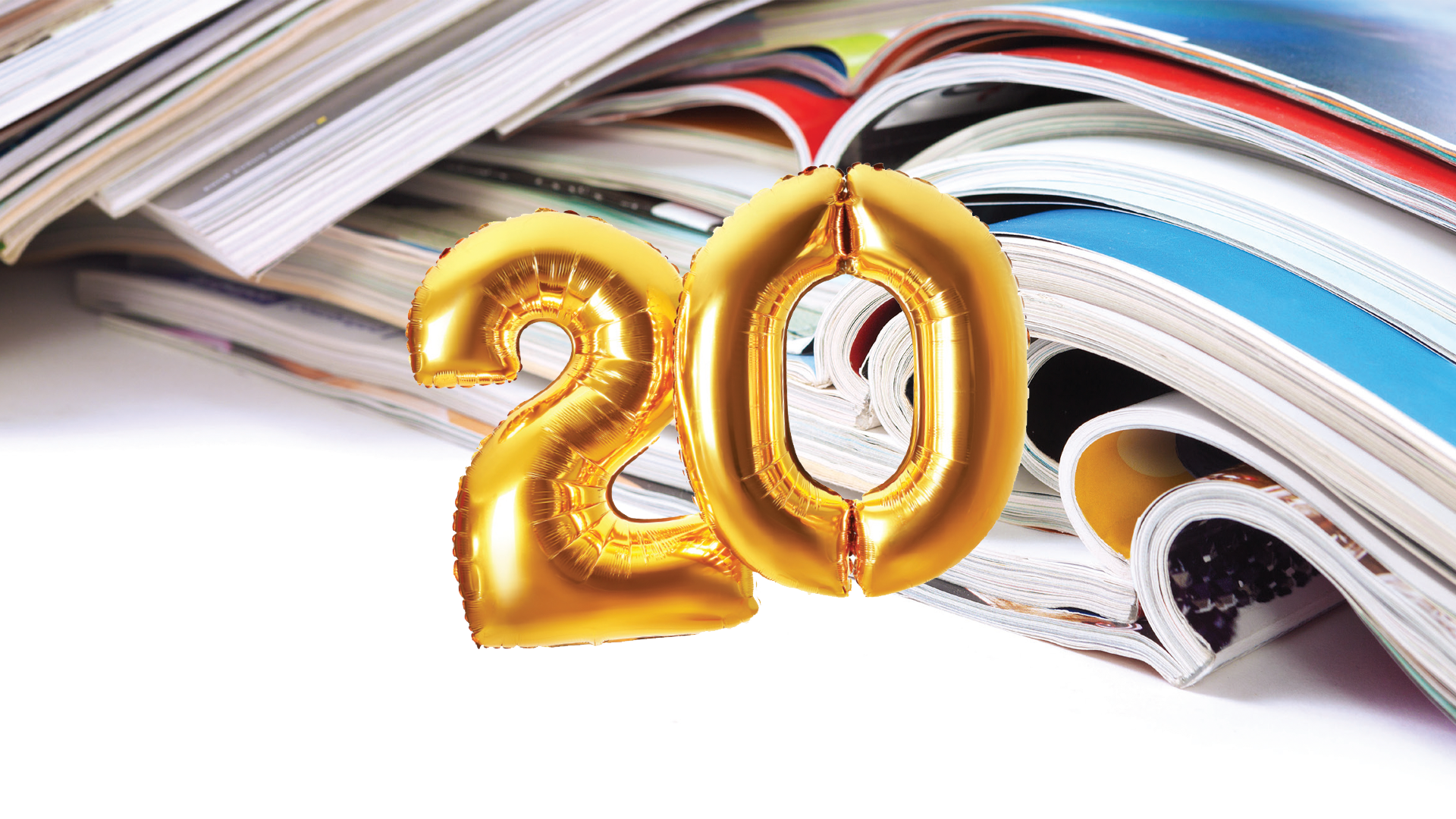 Gold metallic number balloons '20' resting on scattered magazines and publications