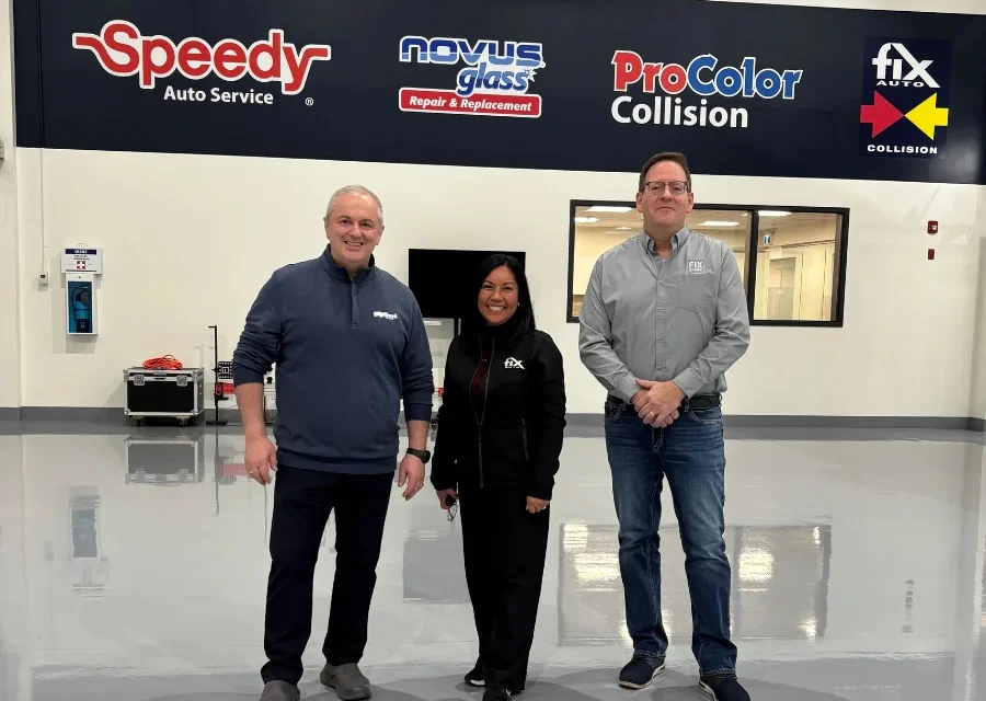 Three professionals standing in automotive service center with Speedy, Novus, ProColor, and Fix Auto logos