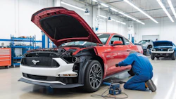 Red Ford Mustang with open hood being serviced in automotive repair workshop