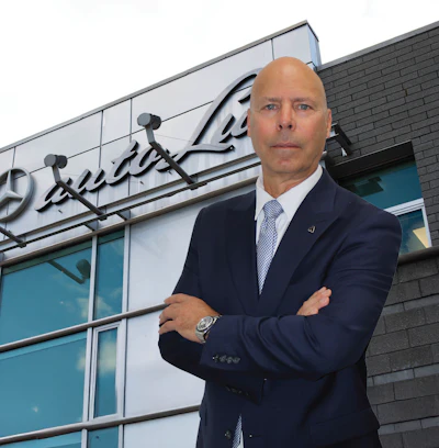 Bald executive in navy suit standing confidently outside Mercedes-Benz corporate building