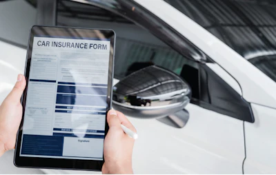 Digital car insurance form on tablet next to white vehicle side mirror