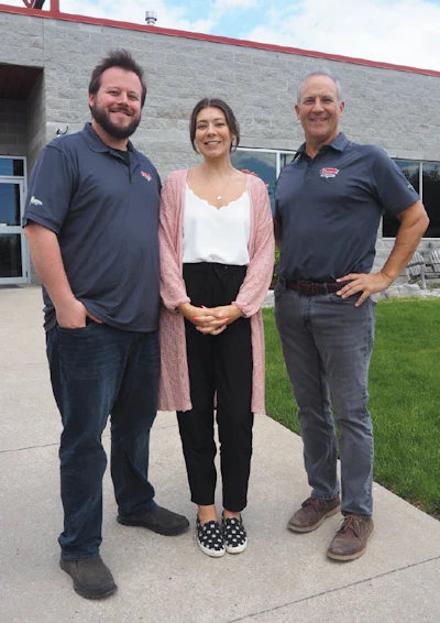 Three professionals standing outside a building, wearing gray company polo shirts