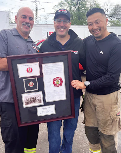 Three firefighters holding a commemorative framed display with historical fire department documents