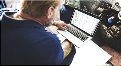 Professional with tattoo working on laptop in workshop or industrial setting