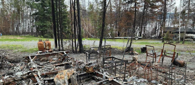 Charred remains of a building site with burned furniture and trees in a forest clearing