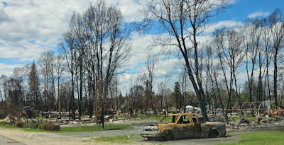 Burned car amid destroyed neighborhood with bare trees and fire damage