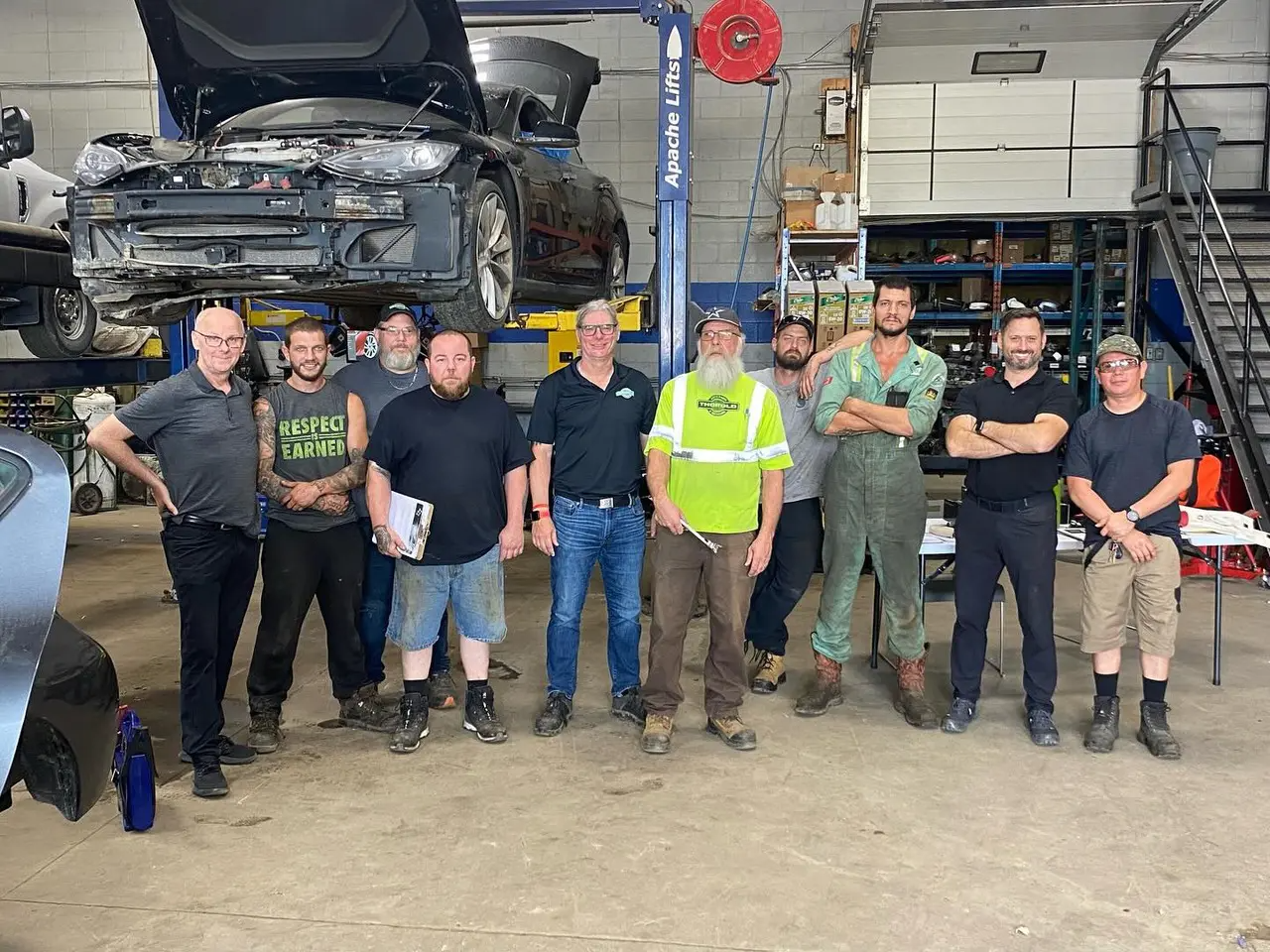 Auto repair team standing together in workshop with vehicle on lift