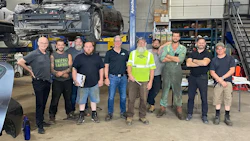 Auto repair team standing together in workshop with vehicle on lift