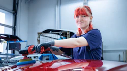 Auto body technician with red hair polishing a red vehicle in a workshop