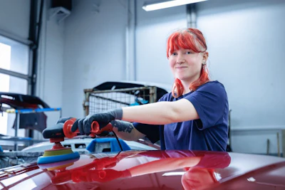 Auto body technician with red hair polishing a red vehicle in a workshop
