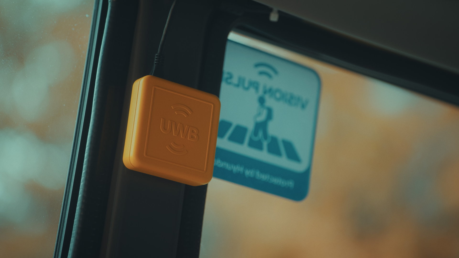 Yellow UWB wireless tag mounted on vehicle window near blue information sign