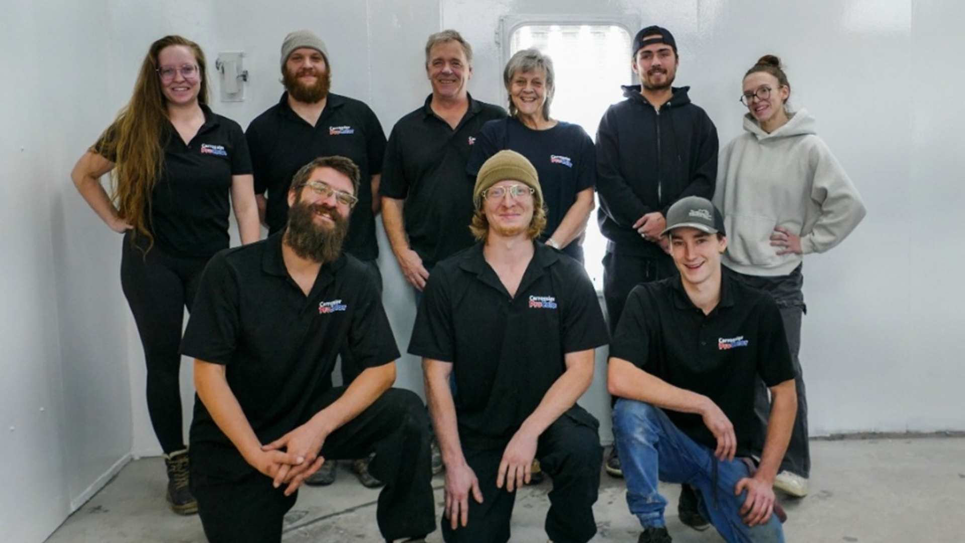 Team of nine professionals in black branded polos posing together indoors for a group photo