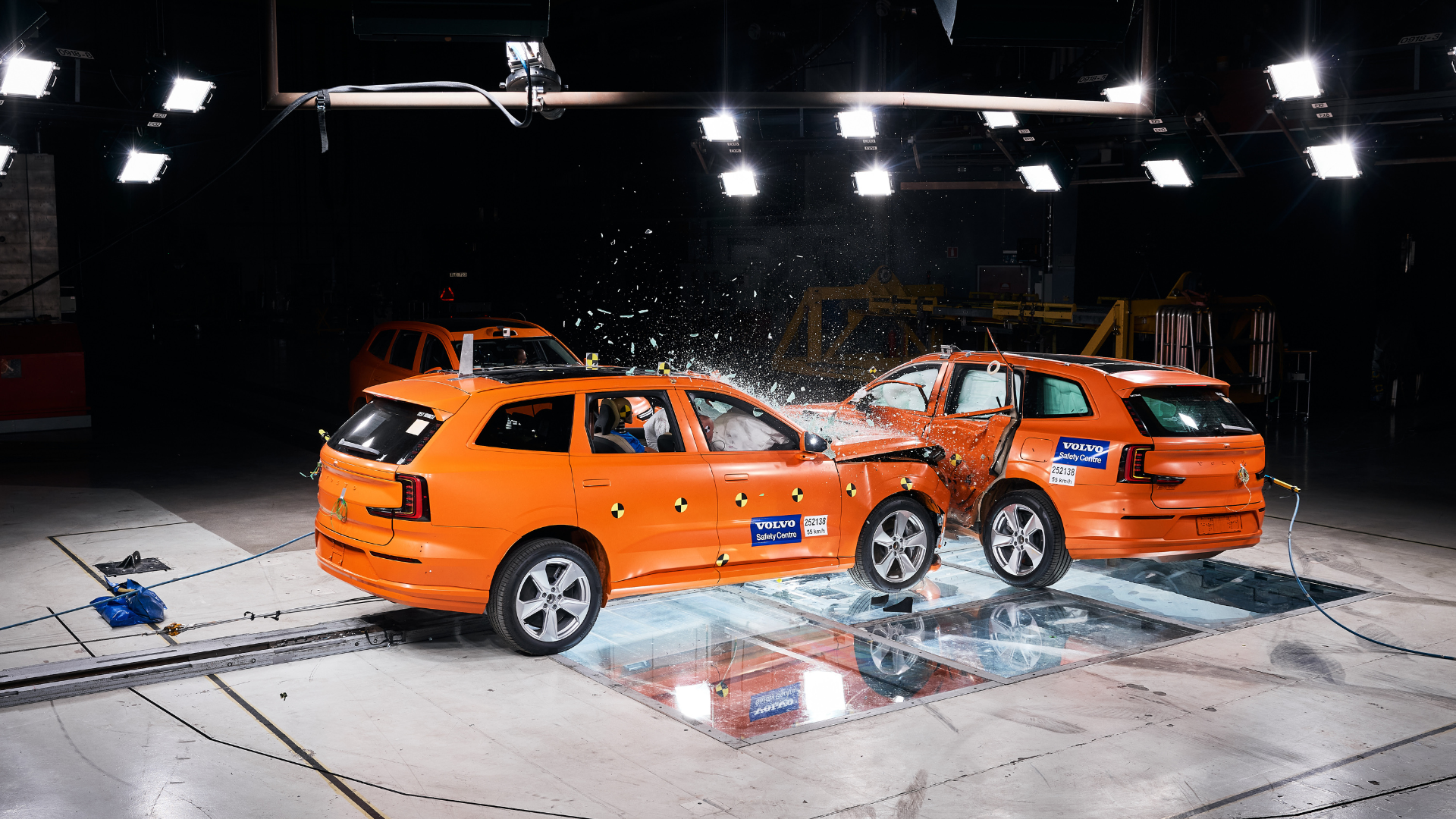 Two orange Volvo vehicles in a crash test collision under bright studio lights