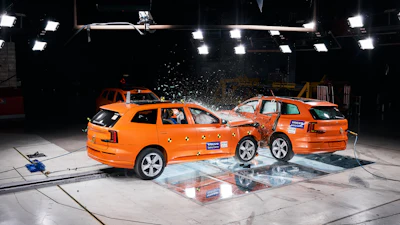 Two orange Volvo vehicles in a crash test collision under bright studio lights