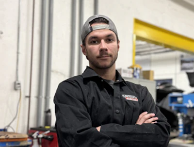 Man in black work shirt with headlamp standing in industrial workshop with arms crossed