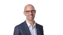 Professional headshot of a smiling man wearing glasses and dark blazer with light blue shirt