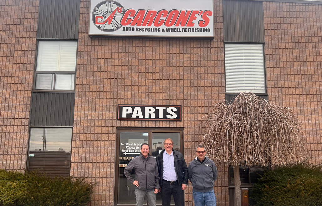 Three men stand outside Cargone's Auto Recycling & Wheel Refinishing storefront with brick facade and signage