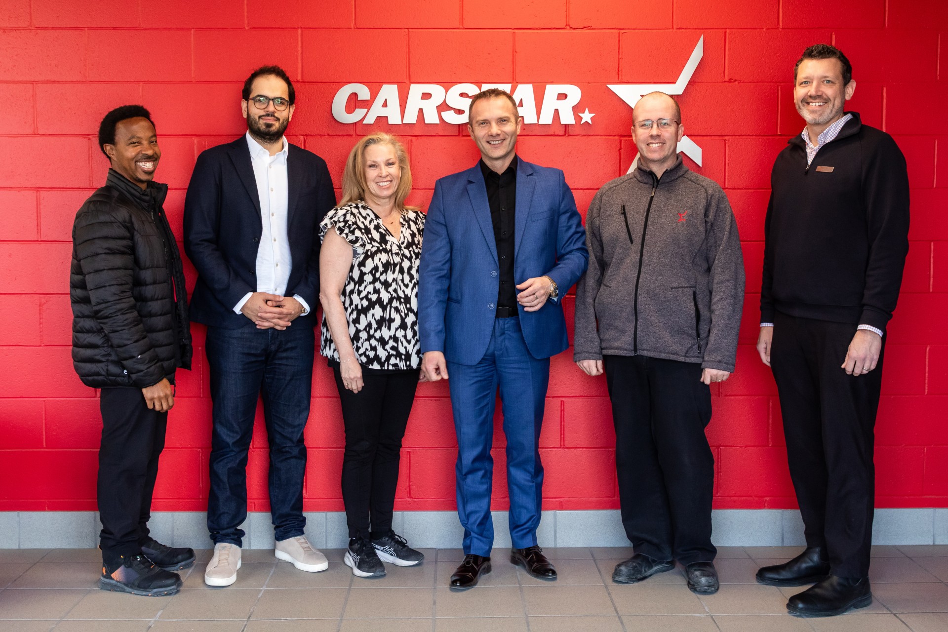 Six professionals posing together in front of red CARSTAR branded wall signage