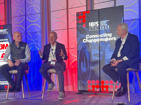 Three professionals participate in a panel discussion at IBIS conference event with 'Connecting Changemakers' branding backdrop.