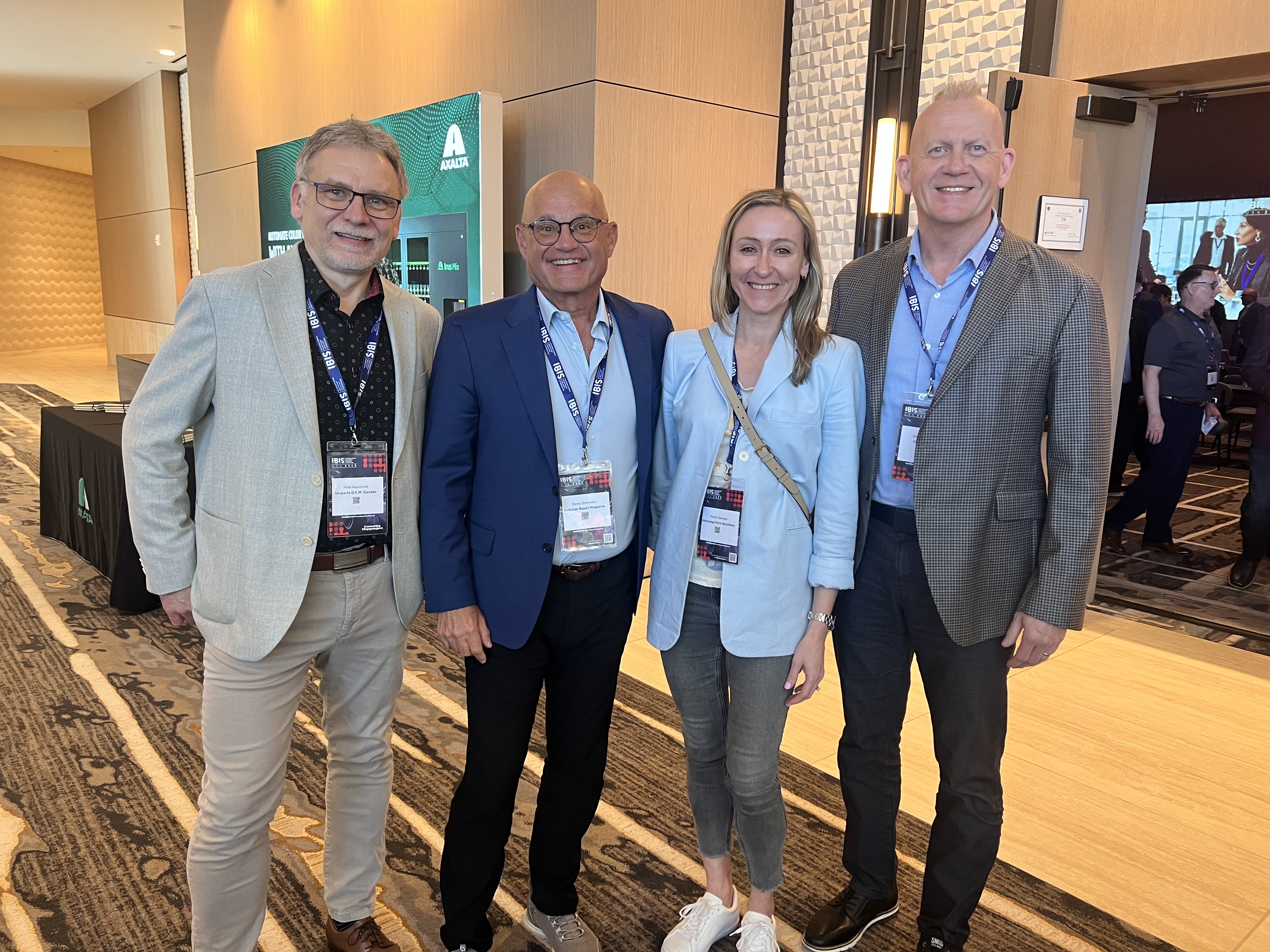 Four professionals wearing conference badges pose together at a corporate event in an indoor venue.