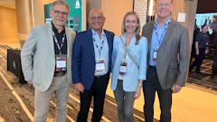 Four professionals wearing conference badges pose together at a corporate event in an indoor venue.
