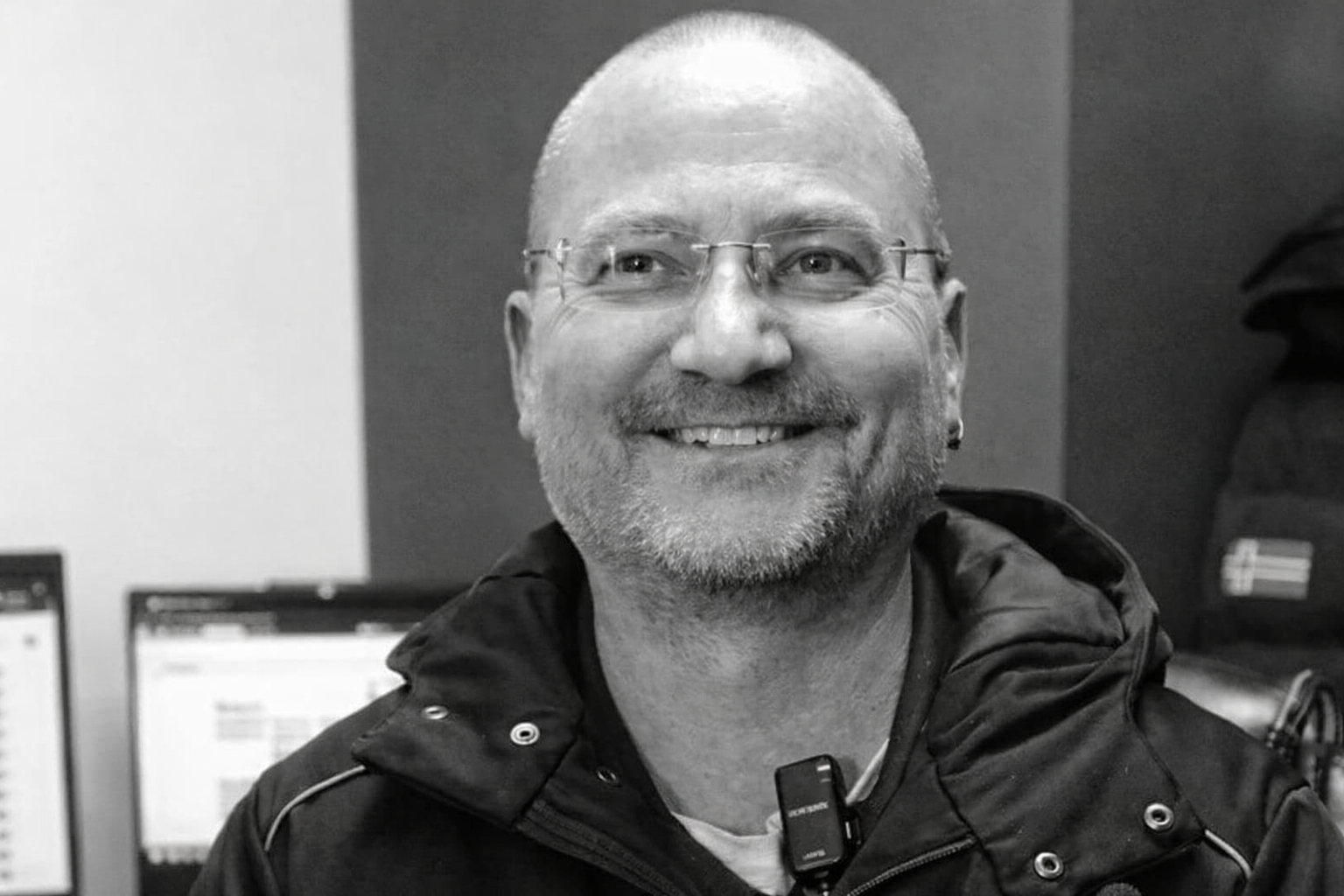 Smiling man with glasses and beard wearing black jacket in office setting