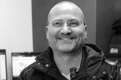 Smiling man with glasses and beard wearing black jacket in office setting