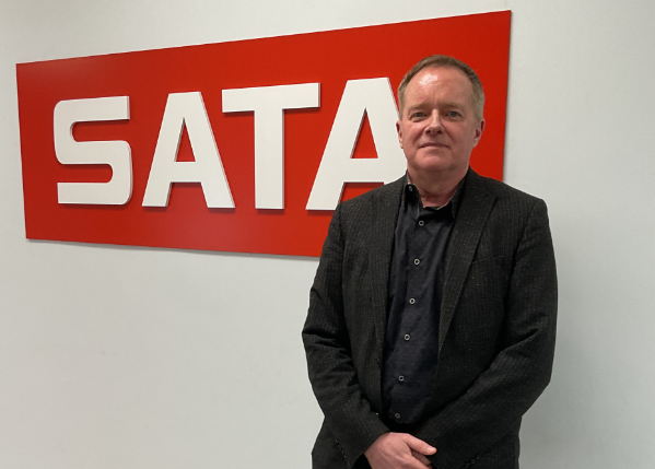 Man in dark blazer standing in front of red SATA company signage