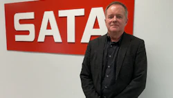 Man in dark blazer standing in front of red SATA company signage