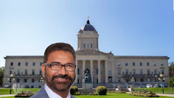 Professional man in glasses and suit smiling in front of Manitoba Legislative Building with dome and manicured grounds