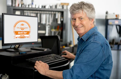 Man in denim shirt smiling at computer displaying Car-Part.com World Tour logo in workshop
