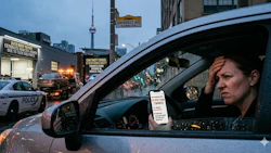 Person in parked car holding parking permit with Toronto police vehicle and urban street scene in background