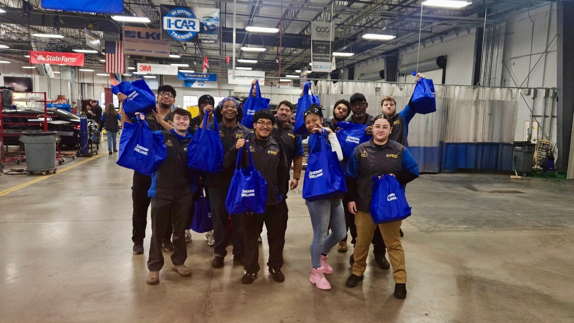 Team of automotive technicians celebrating in blue branded jackets at an industrial warehouse facility
