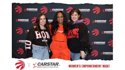 Three women pose together at a Toronto Raptors Women's Empowerment Night event sponsored by CARSTAR, wearing team apparel against branded backdrop.