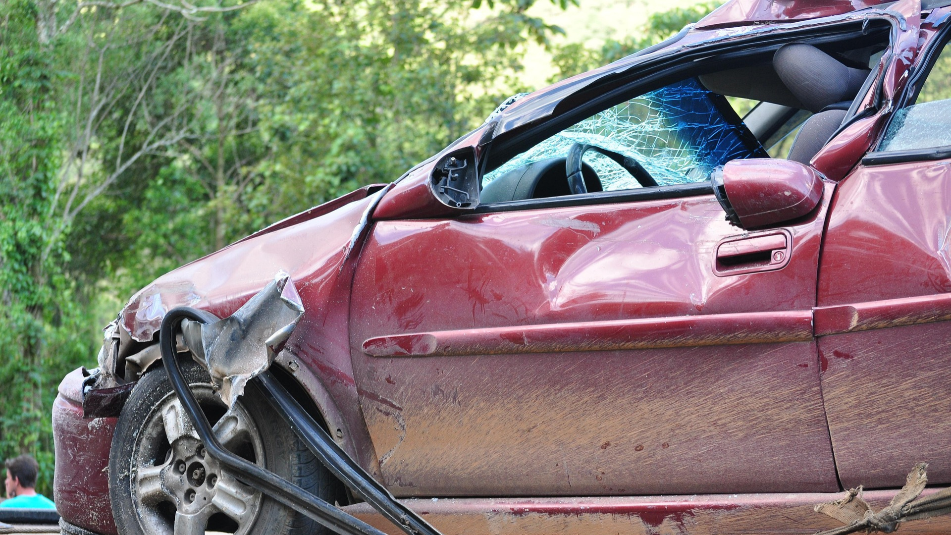 Severely damaged maroon sedan with crushed front end and deployed airbag after collision