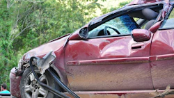 Severely damaged maroon sedan with crushed front end and deployed airbag after collision