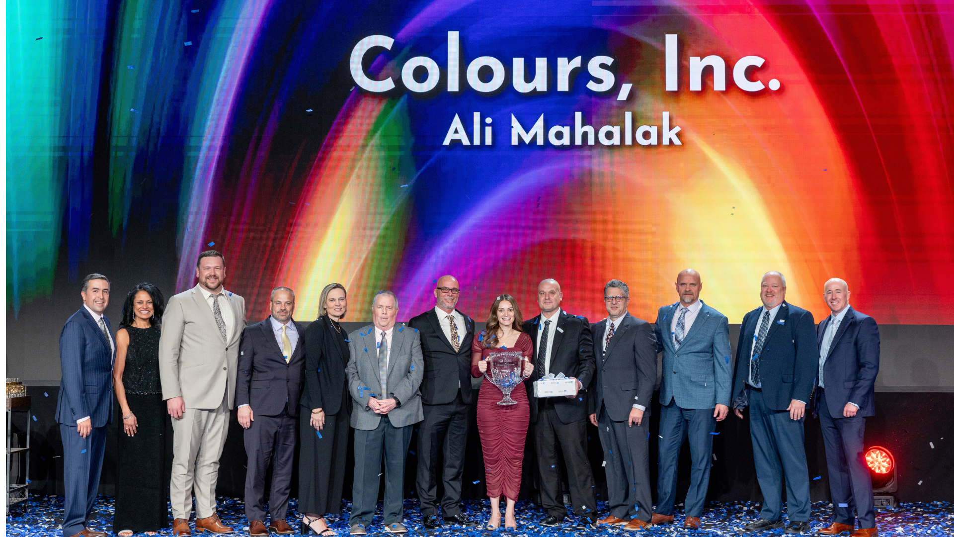 Group of business professionals at corporate event with colorful gradient backdrop displaying Colours, Inc. branding