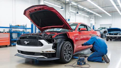 Mechanic in blue uniform servicing red Ford Mustang with open hood in modern automotive service facility