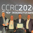Four men in business attire at CCRC2026 awards event, one holding a certificate and trophy