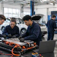 Automotive technicians inspect an electric vehicle battery pack in a repair facility workshop.