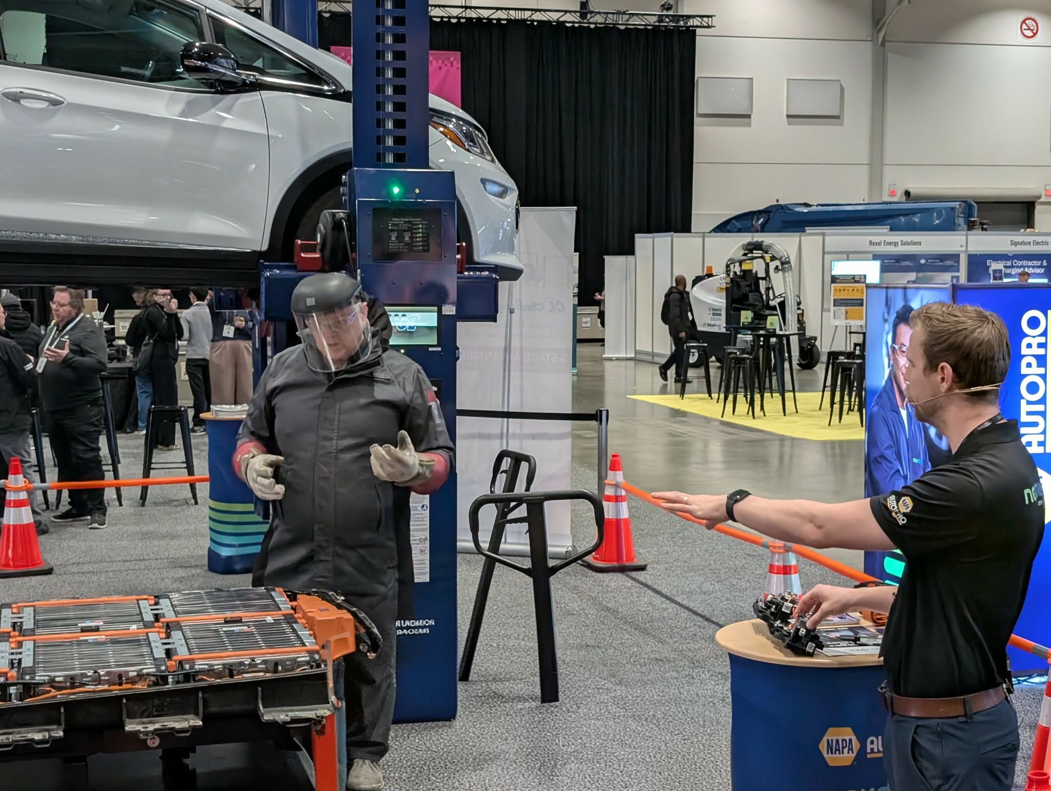 Attendees interact at an automotive trade show with vehicle lifts and NAPA branded booth visible