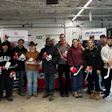 Large group of people posing together in an industrial garage with red and white decorative items, standing in front of corporate signage.