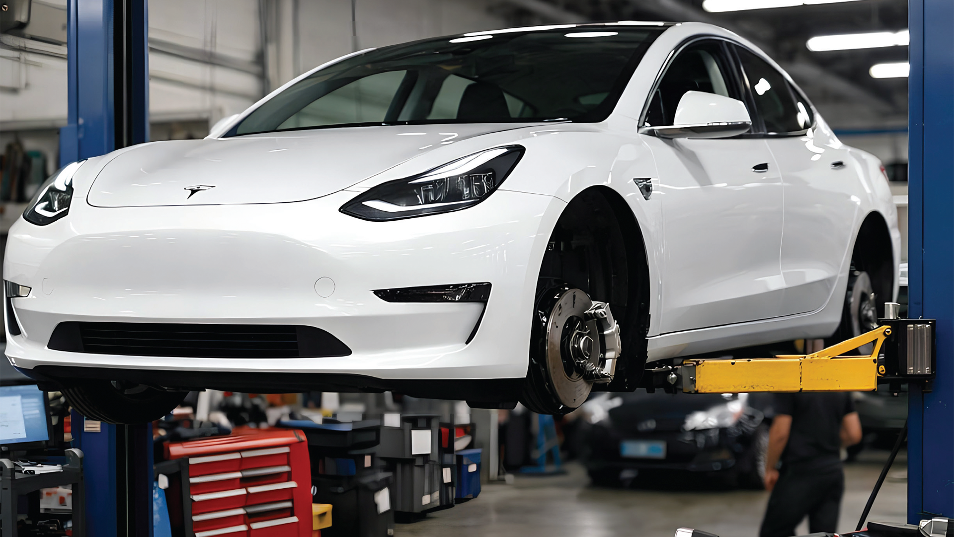 White Tesla Model 3 elevated on blue service lift in automotive workshop with tools and equipment visible
