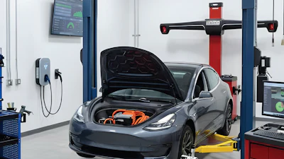 Tesla electric vehicle undergoing service in a modern automotive repair facility with diagnostic equipment and wheel alignment machine