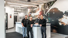 Four team members in black shirts standing at a modern white reception desk in a bright office space