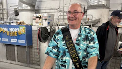 Man wearing turquoise Hawaiian shirt and sash smiling in industrial warehouse facility